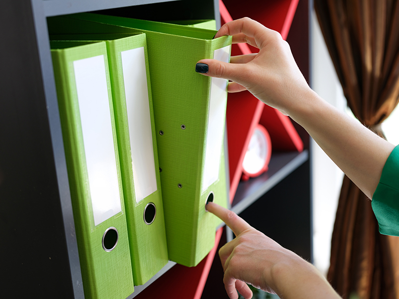 Close-up of woman taking off green folder with documents from shelf. Archive and office work. Business and workplace organization concept